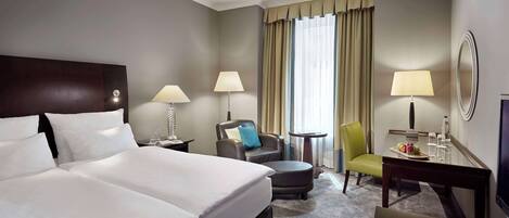 A hotel room with a large bed, two bedside tables with lamps, a desk with a chair, a small round table, and a television.