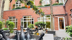 A courtyard with a metal bucket of champagne bottles, a brick building with large windows, and outdoor seating.