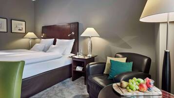 A hotel room with a bed, a desk, a leather chair, a table with fruit, and two lamps.