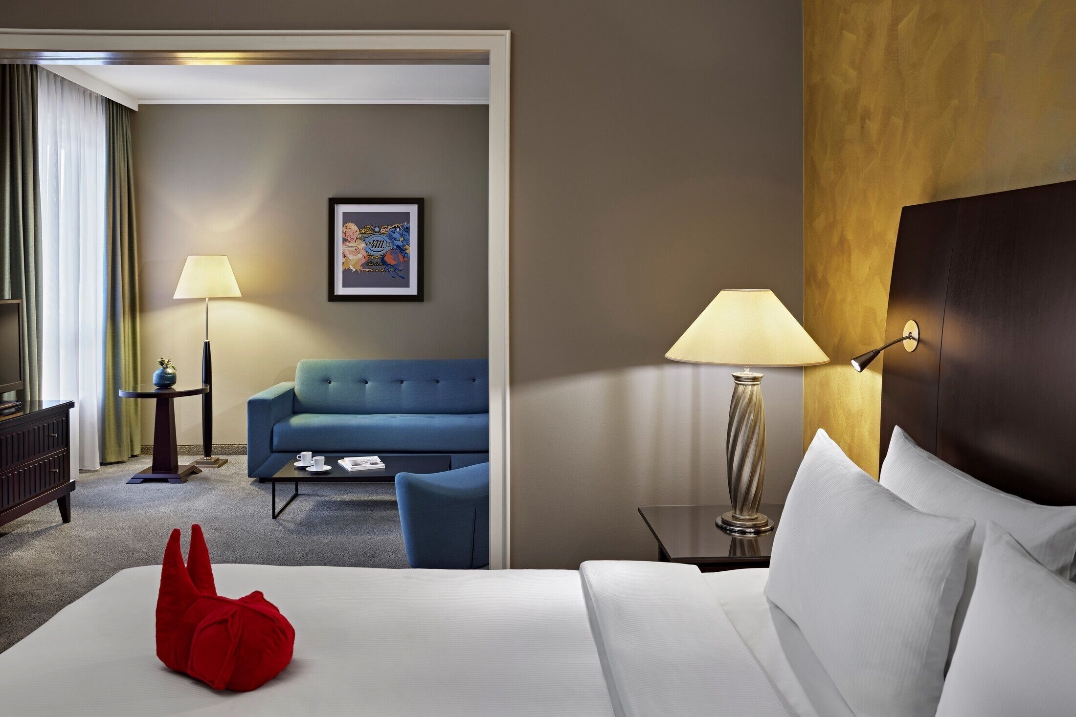 A hotel room with a bed, a blue sofa, a small table, a lamp, and a framed picture on the wall.