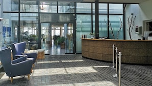 A modern lobby with a reception desk, seating area, and a glass entrance leading to an outdoor space.