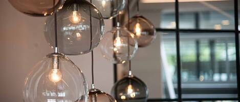 A series of spherical glass pendant lights with exposed bulbs, hanging from a ceiling in a modern interior space with large windows.
