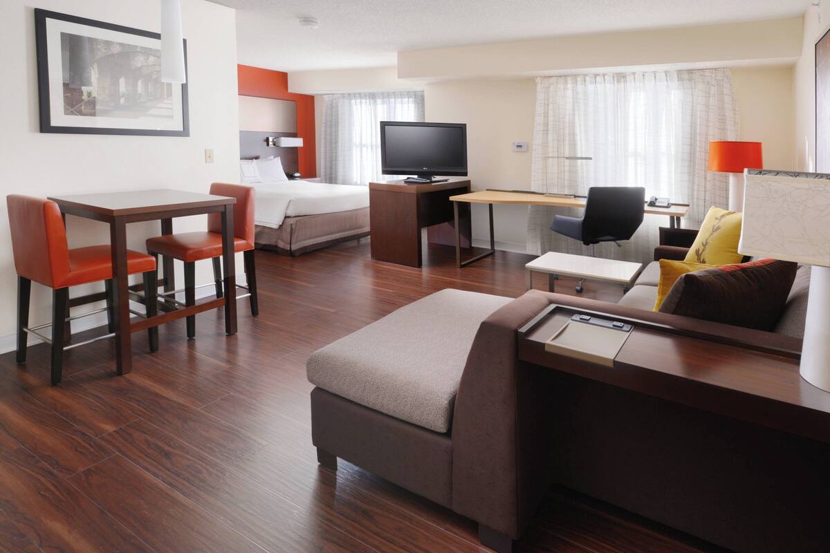 Ein Hotelzimmer mit Bett, Schreibtisch, Stuhl, Fernseher und einer kleinen Sitzecke.