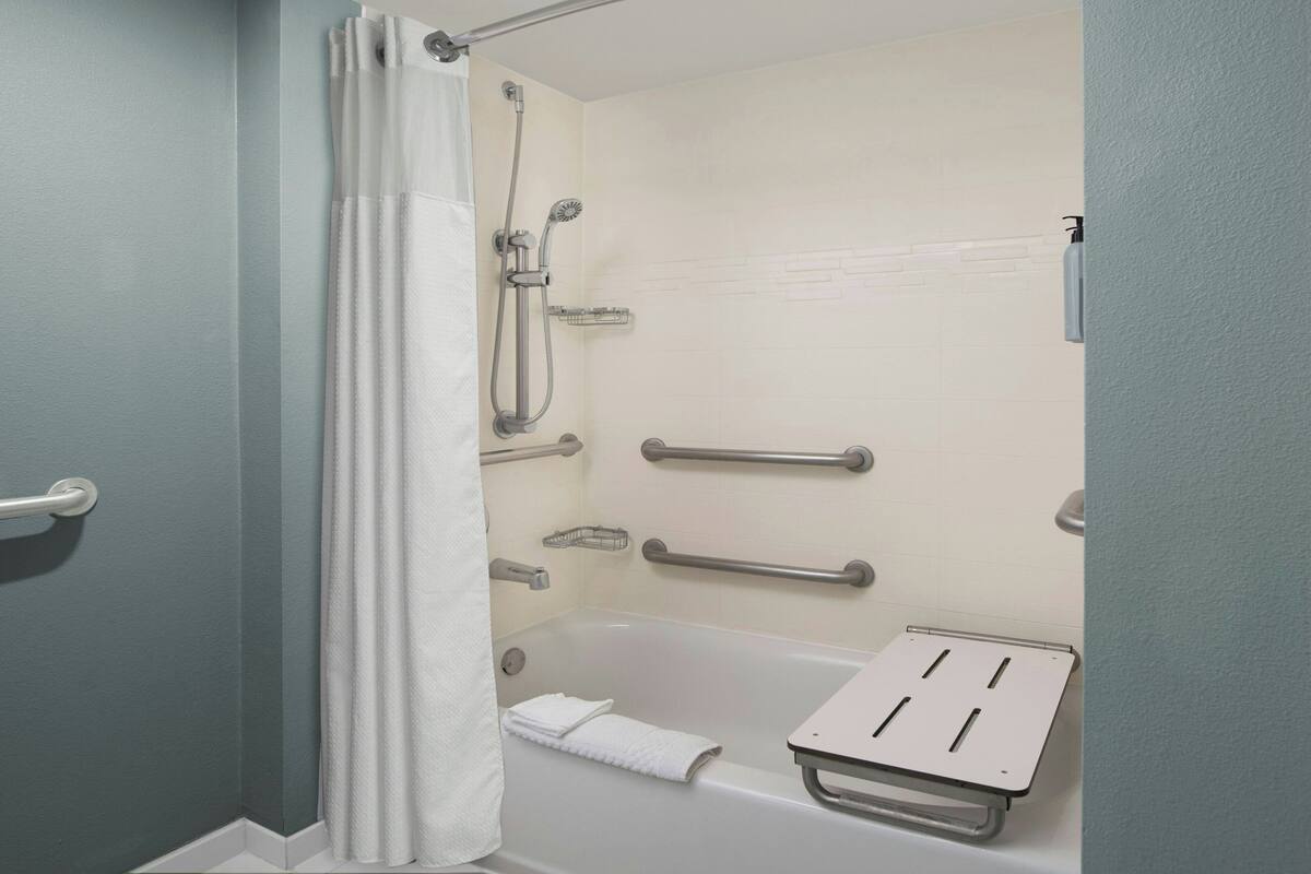 Ein Badezimmer mit Badewanne, Dusche und Haltegriffen.