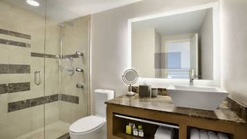 Un baño moderno con ducha envuelta en vidrio, inodoro blanco, encimera de mármol con lavabo sobre encimera y un espejo grande.