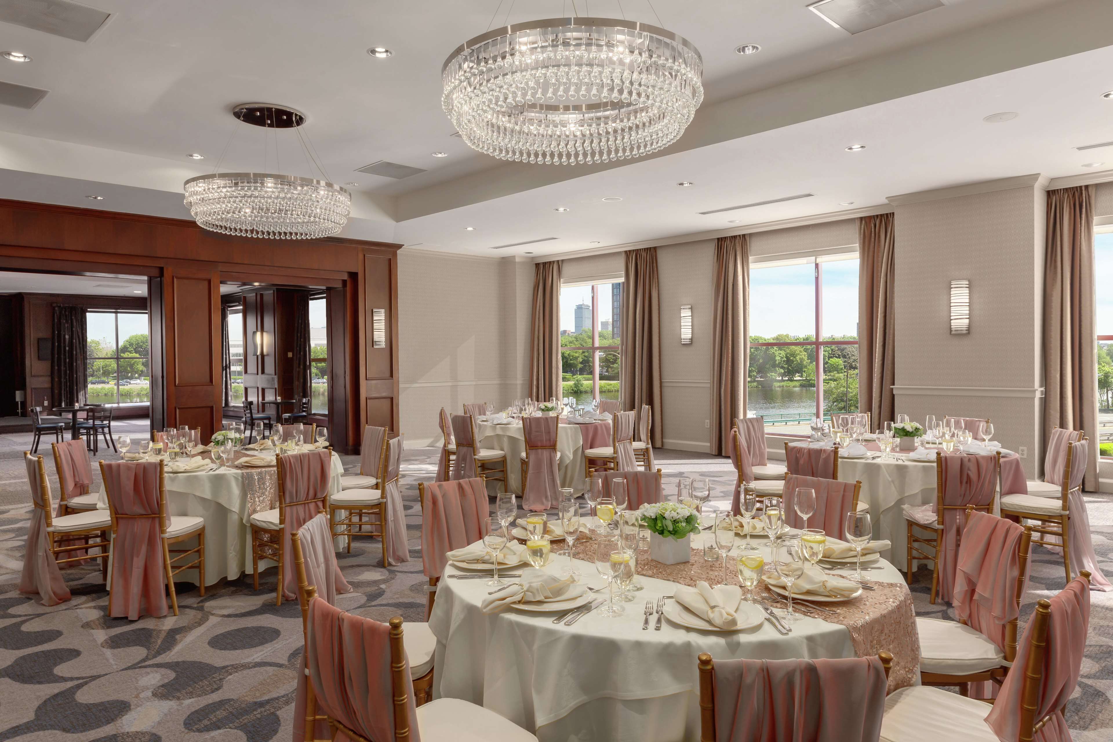 A banquet hall with round tables set for dining, chandeliers, and large windows with views.