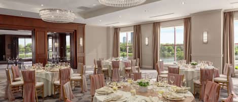 A banquet hall with round tables set for dining, chandeliers, and large windows with views.