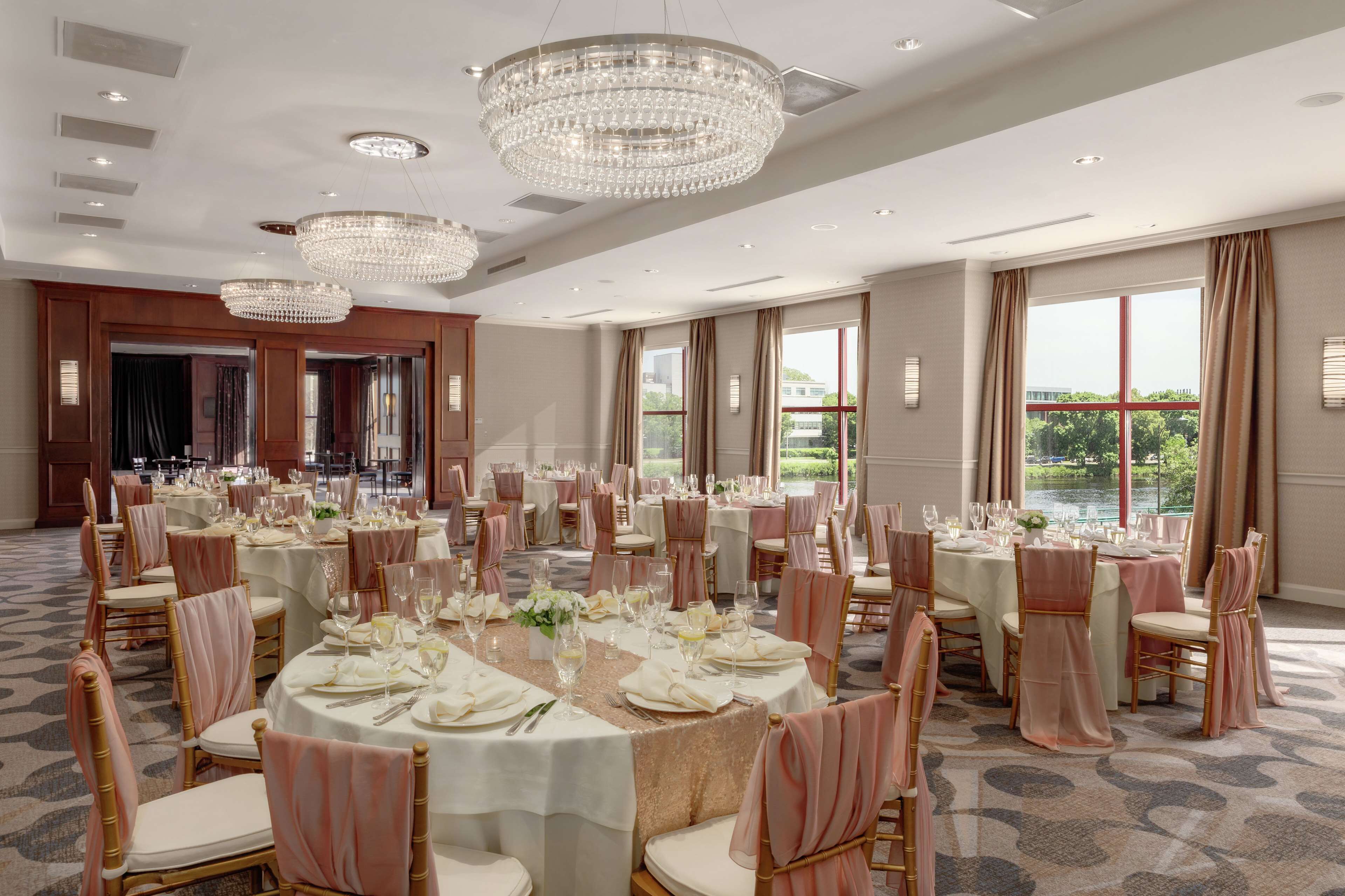 A banquet hall with round tables, chandeliers, and large windows offering a view.