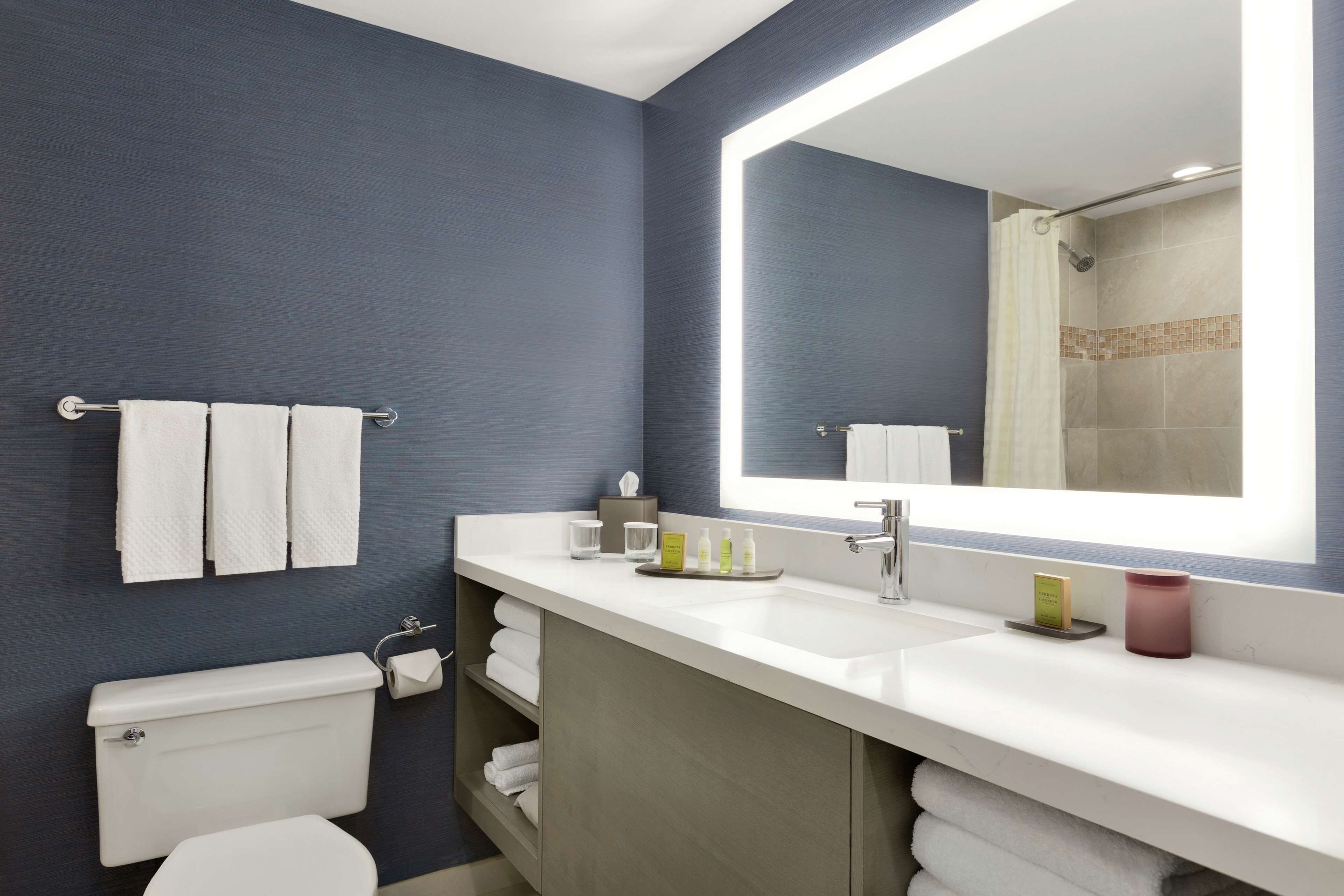Un baño moderno con un espejo grande, lavamanos blanco y un inodoro.