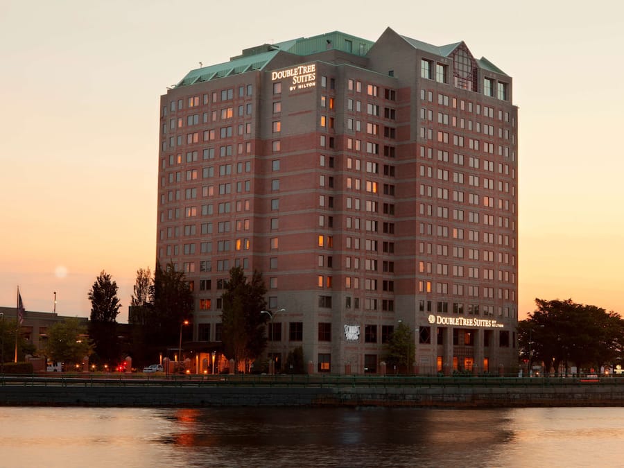 A high-rise hotel with multiple floors, a prominent sign reading "DoubleTree Suites by Hilton," and a waterfront view.