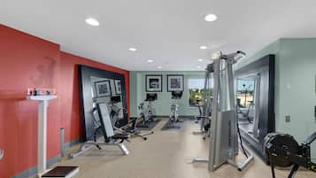 Uma academia com aparelhos de cardio, estações de musculação e um painel de espelhos.