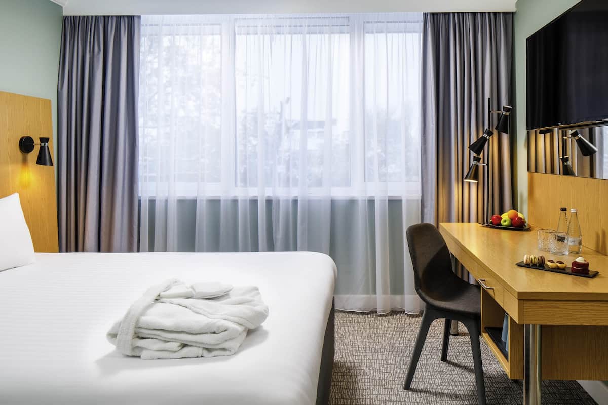 A hotel room with a bed, a desk, a chair, a TV, and a window with curtains.