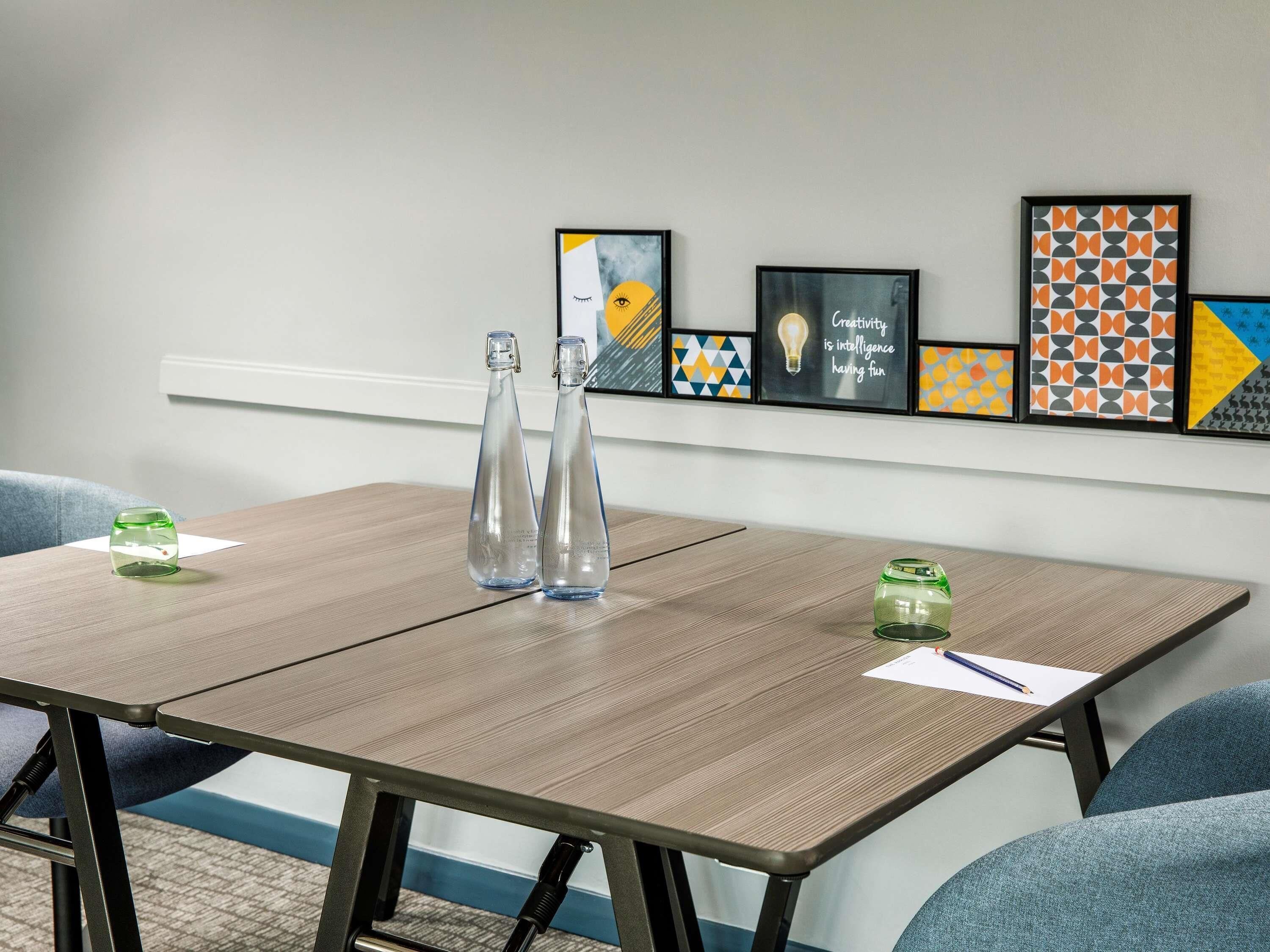 A conference room with a wooden table, two clear glass bottles, and framed artwork on the wall.