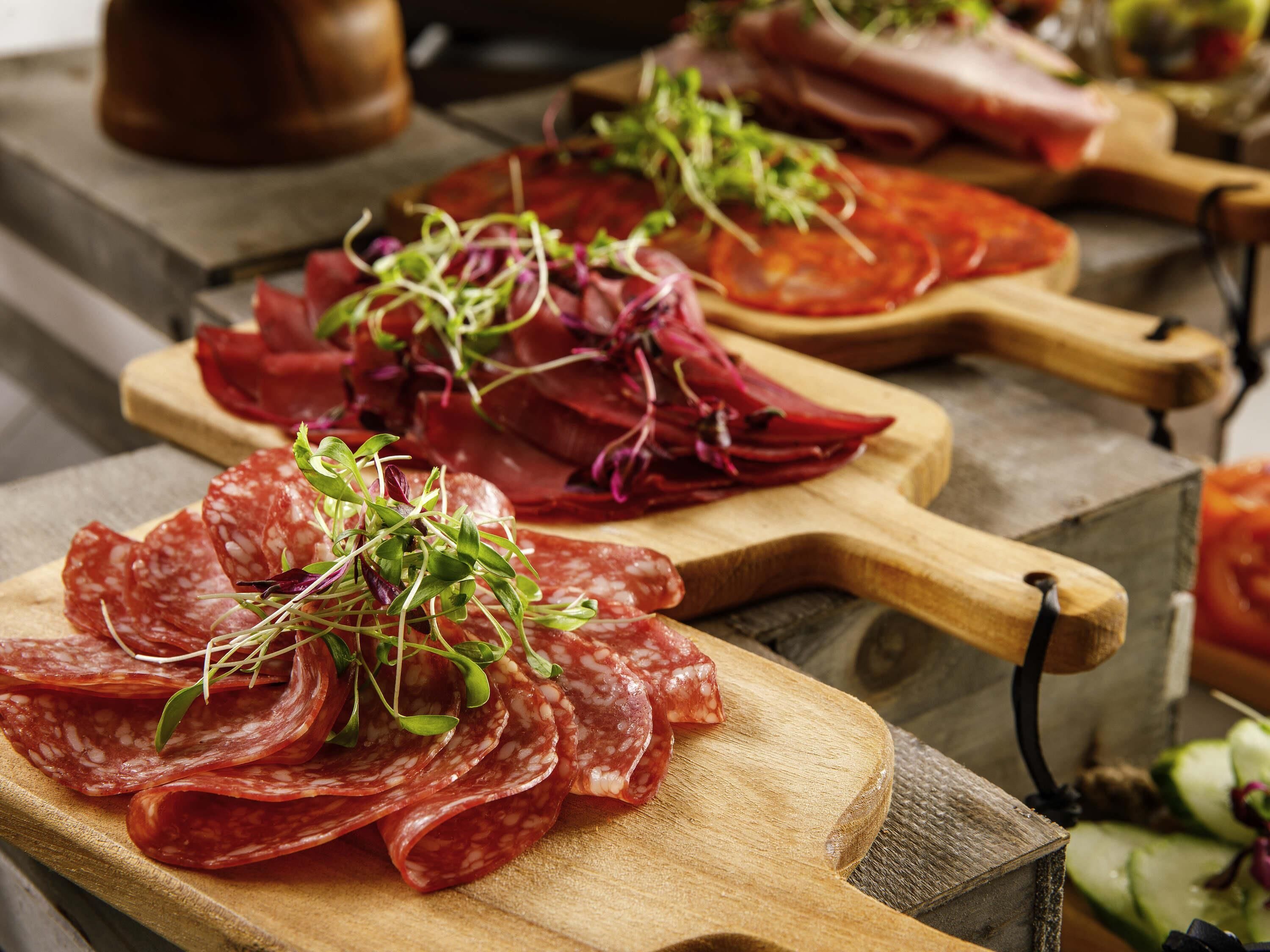 A wooden cutting board with sliced salami and red cabbage garnished with greens.
