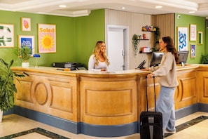 Een hotel receptiebalie met een groene wand, ingelijste kunst en een houten toonbank.
