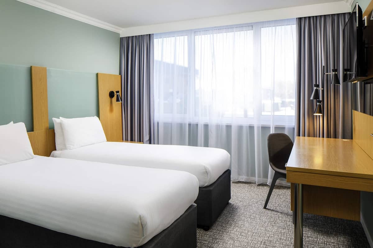 A hotel room with two beds, a desk, a chair, and a TV.