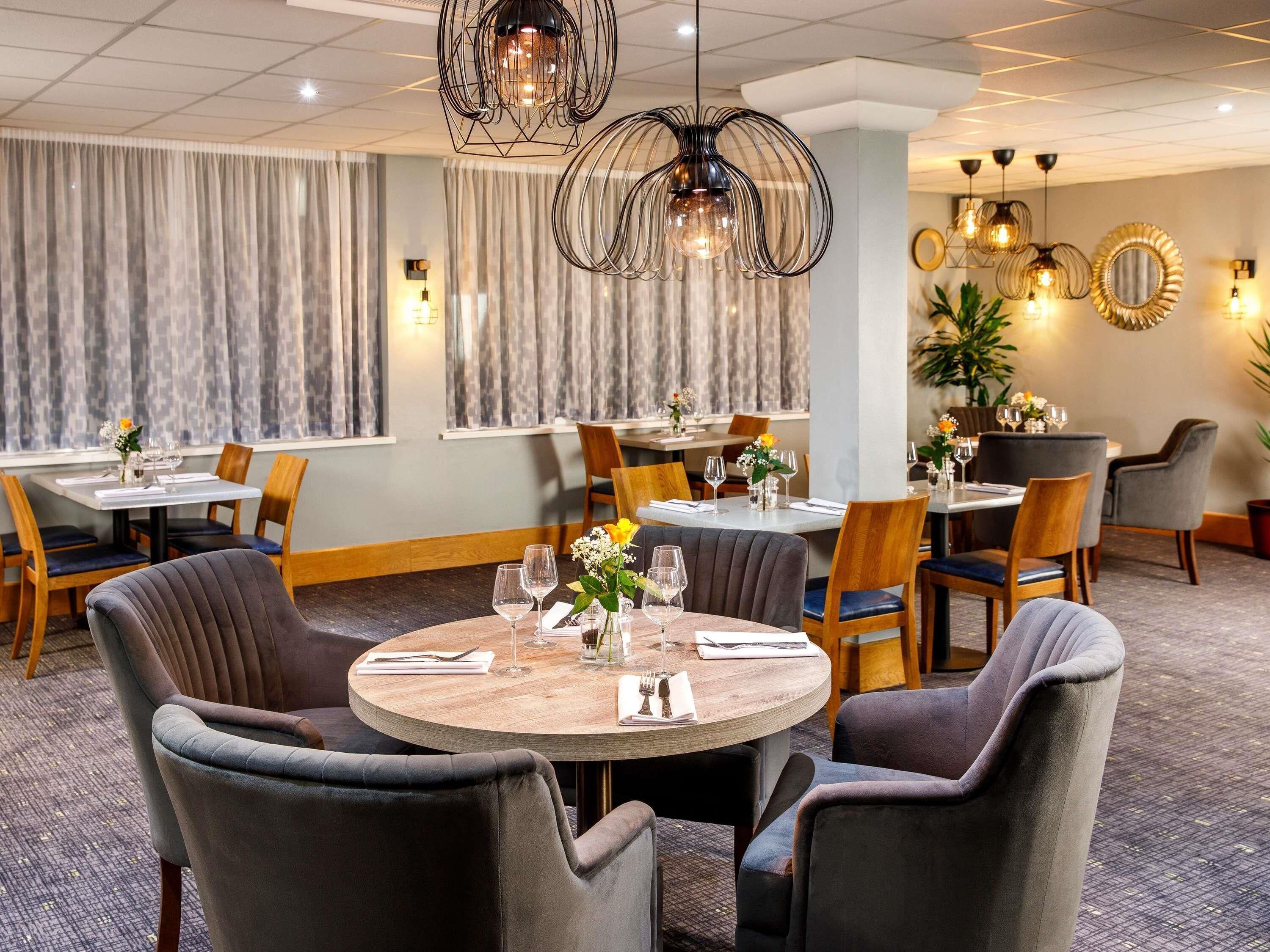A restaurant with round tables, chairs, and hanging pendant lights.