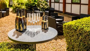 A round table with bottles and glasses, surrounded by outdoor seating and greenery. - The Harlow Hotel By AccorHotels (Harlow)