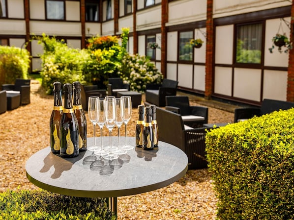 Une table ronde, ornée de bouteilles et de verres, entourée de siÚges et de verdure, le tout installé en plein air.