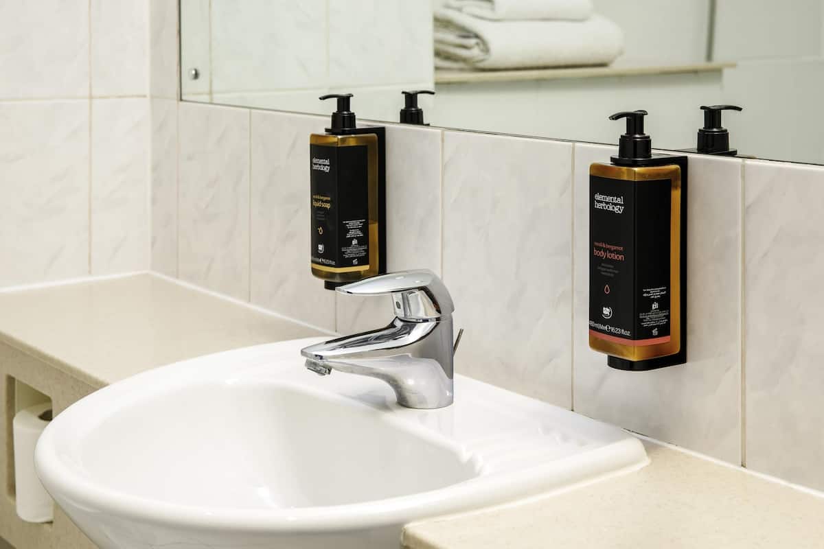 A bathroom with a white sink, a chrome faucet, and two soap dispensers mounted on the wall.