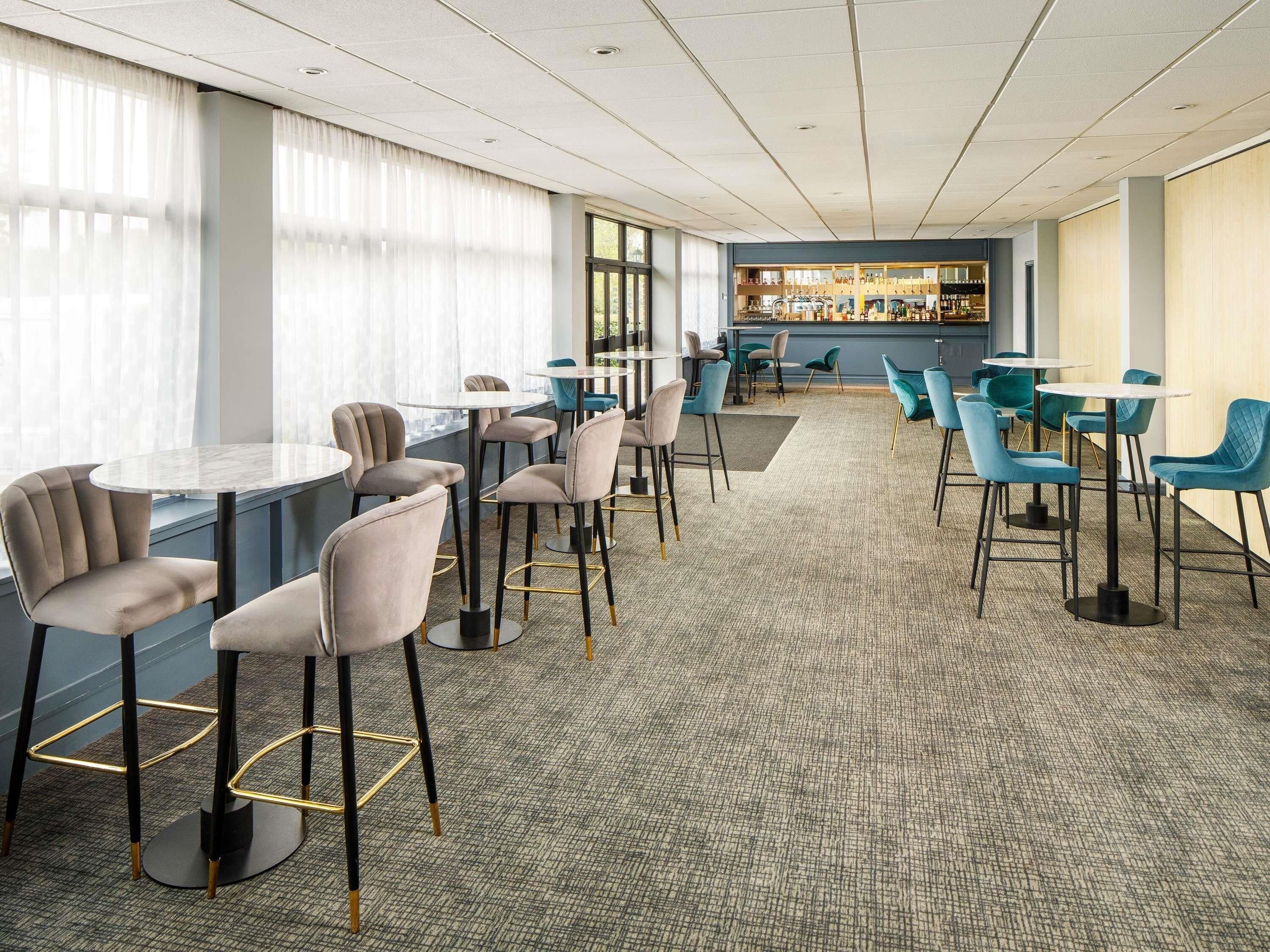 A hotel lobby with round tables and chairs, a bar area, and large windows.