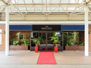 La entrada del The Harlow Hotel, con alfombra roja, plantas en macetas y fachada de ladrillo.