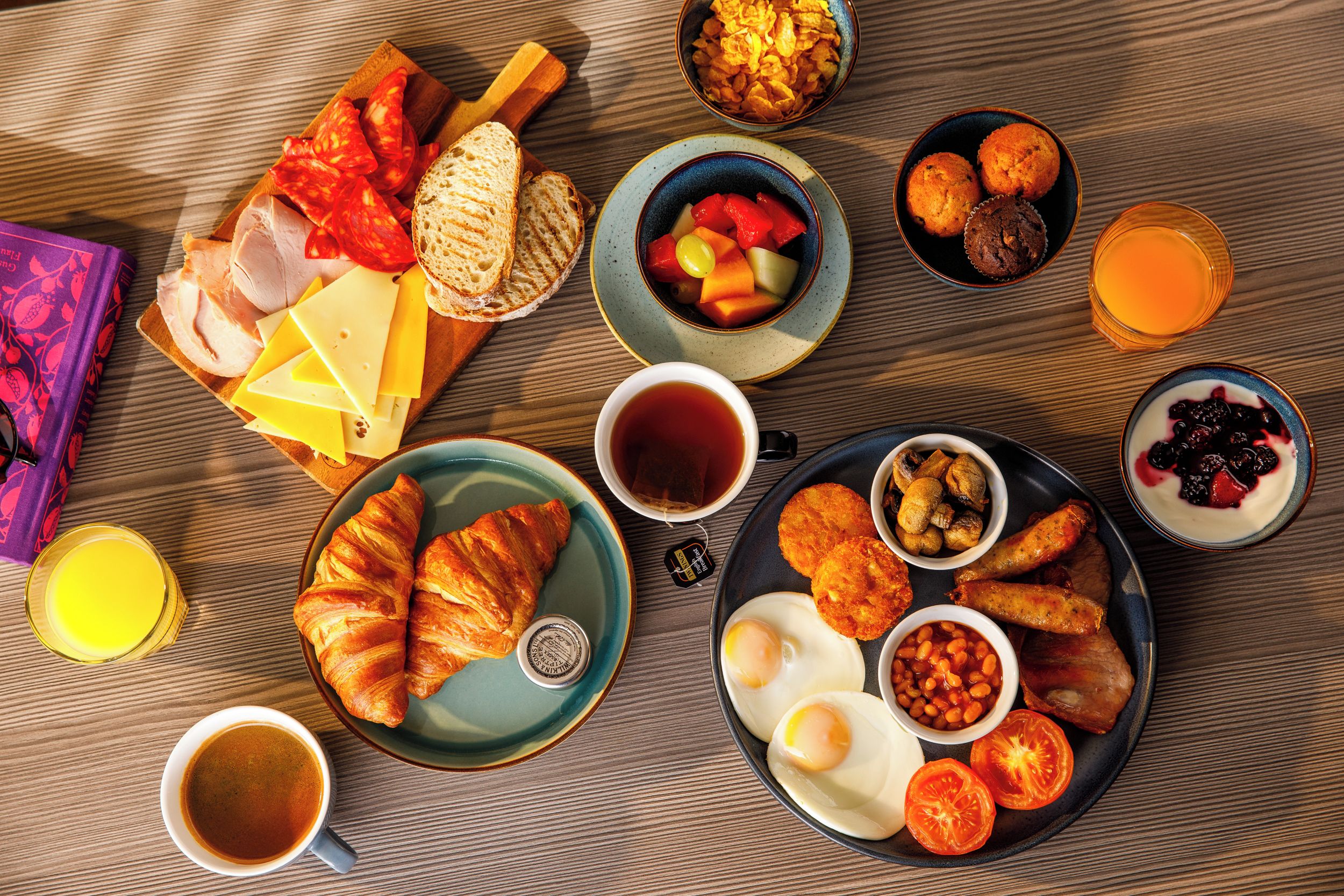 A breakfast spread with various foods and drinks on a wooden table.