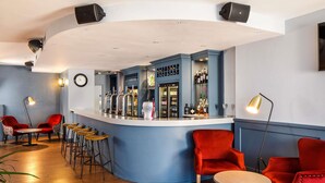 A bar area with a curved counter, red chairs, stools, and a clock on the wall. - The Harlow Hotel By AccorHotels (Harlow)