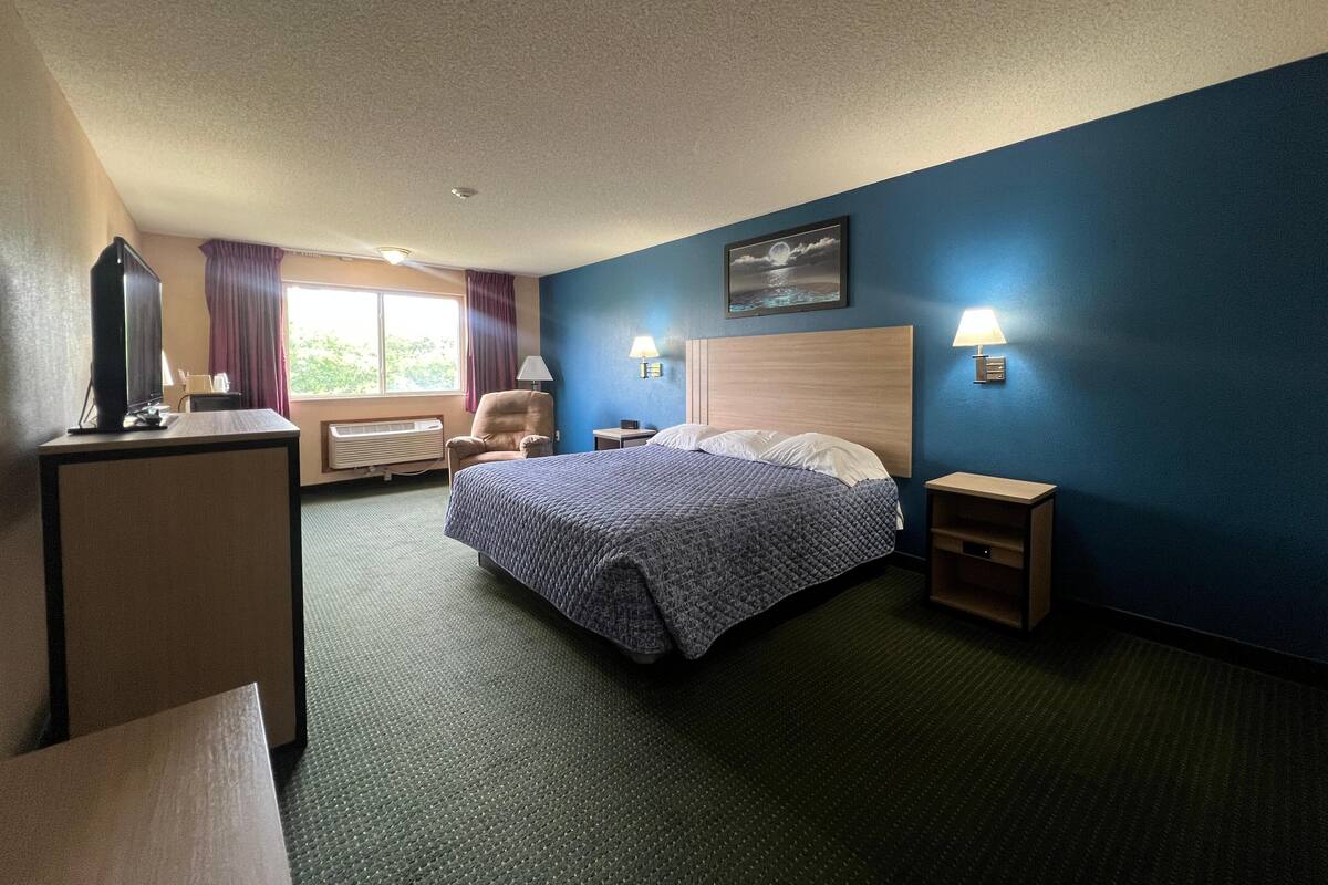 Una habitación de hotel con cama, una silla, un escritorio y una ventana con cortinas.