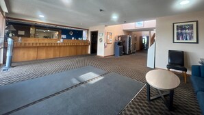 Eine Hotelhalle mit Rezeption, einer Sitzecke mit Tisch und Stühlen sowie einem Korridor zu weiteren Zimmern.