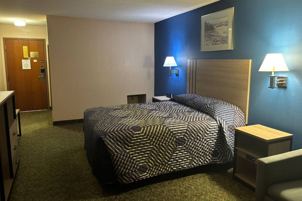 Una habitación de hotel con una cama grande, dos mesitas de noche, un escritorio y una silla.
