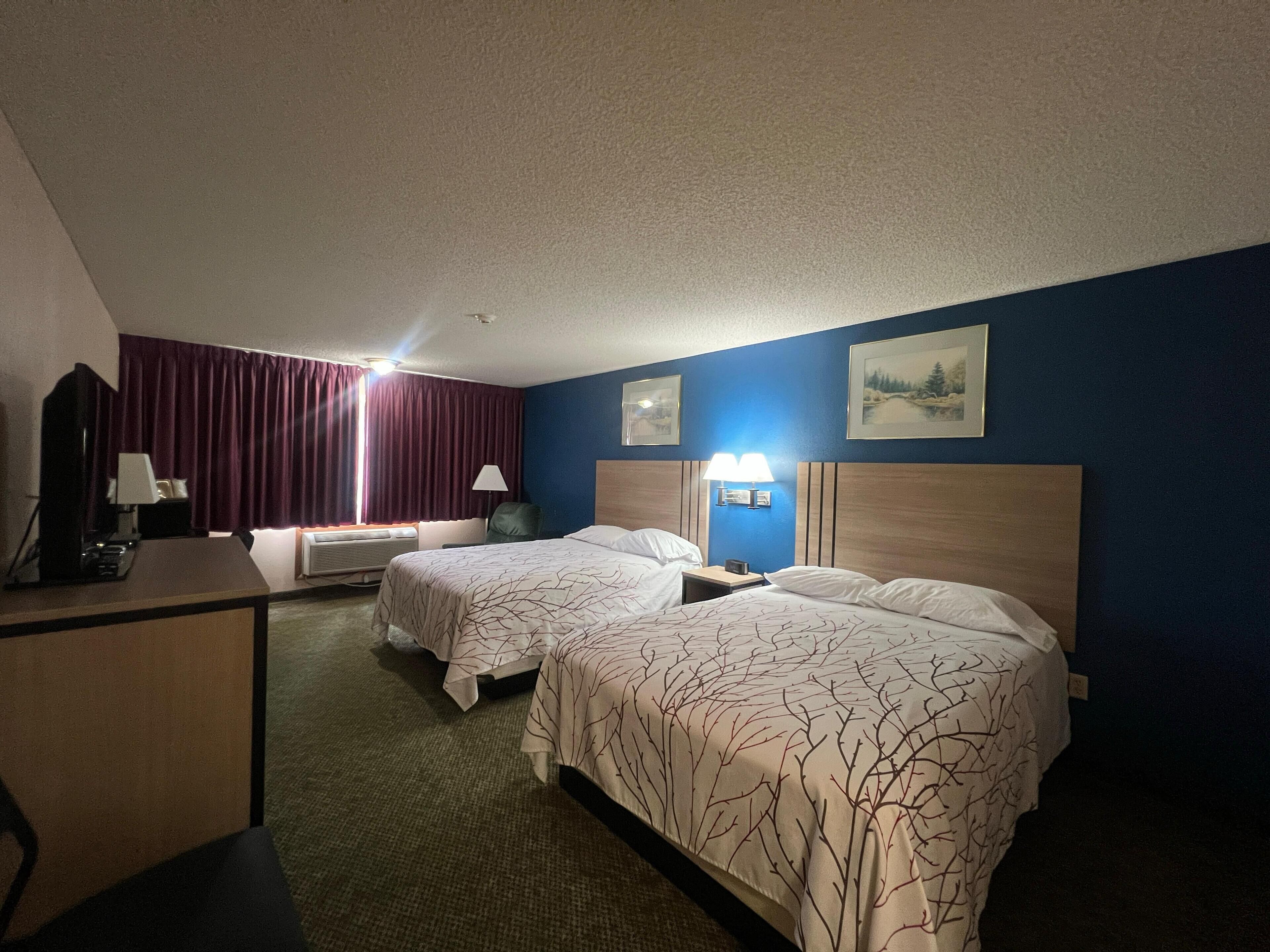 A hotel room with two beds, a desk, a chair, a lamp, and a picture on the wall.