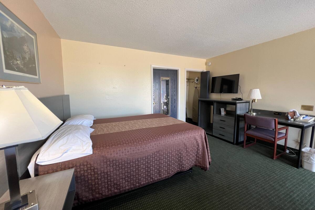 Una habitación de hotel con una cama, un escritorio, una silla, un televisor y una lámpara.