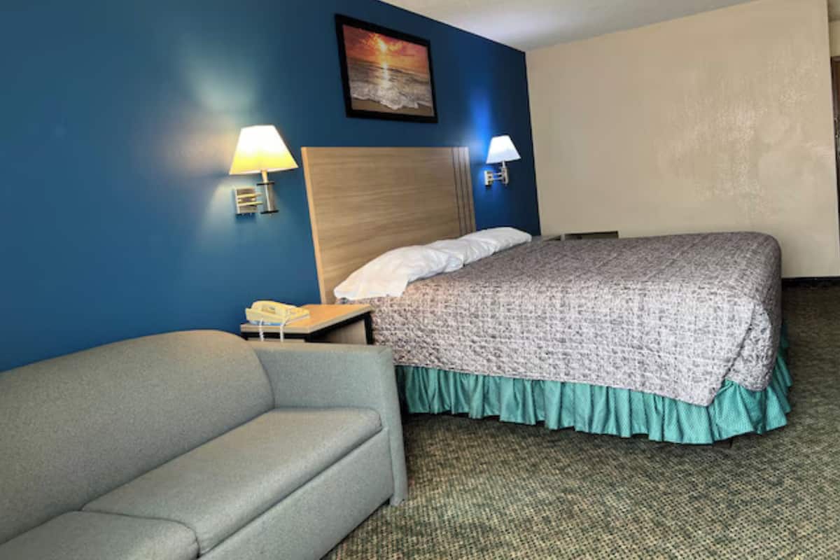Una habitación de hotel con una cama, una mesita de noche, una lámpara y un sofá.
