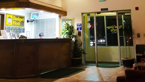 A reception area with a counter, a sign for 'Budget Host', a plant, and a glass door leading outside. - Budget Host Royal Gorge Inn (Canon City)