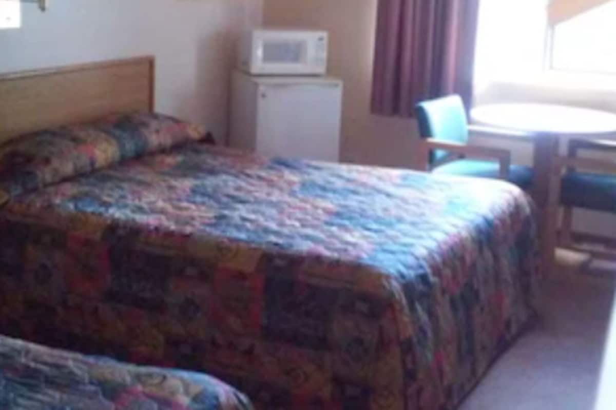 A hotel room with two beds, a desk, a chair, a microwave, and a window with curtains.