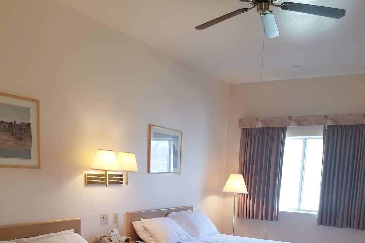 A hotel room with two beds, a ceiling fan, bedside lamps, a telephone, and a window with curtains.