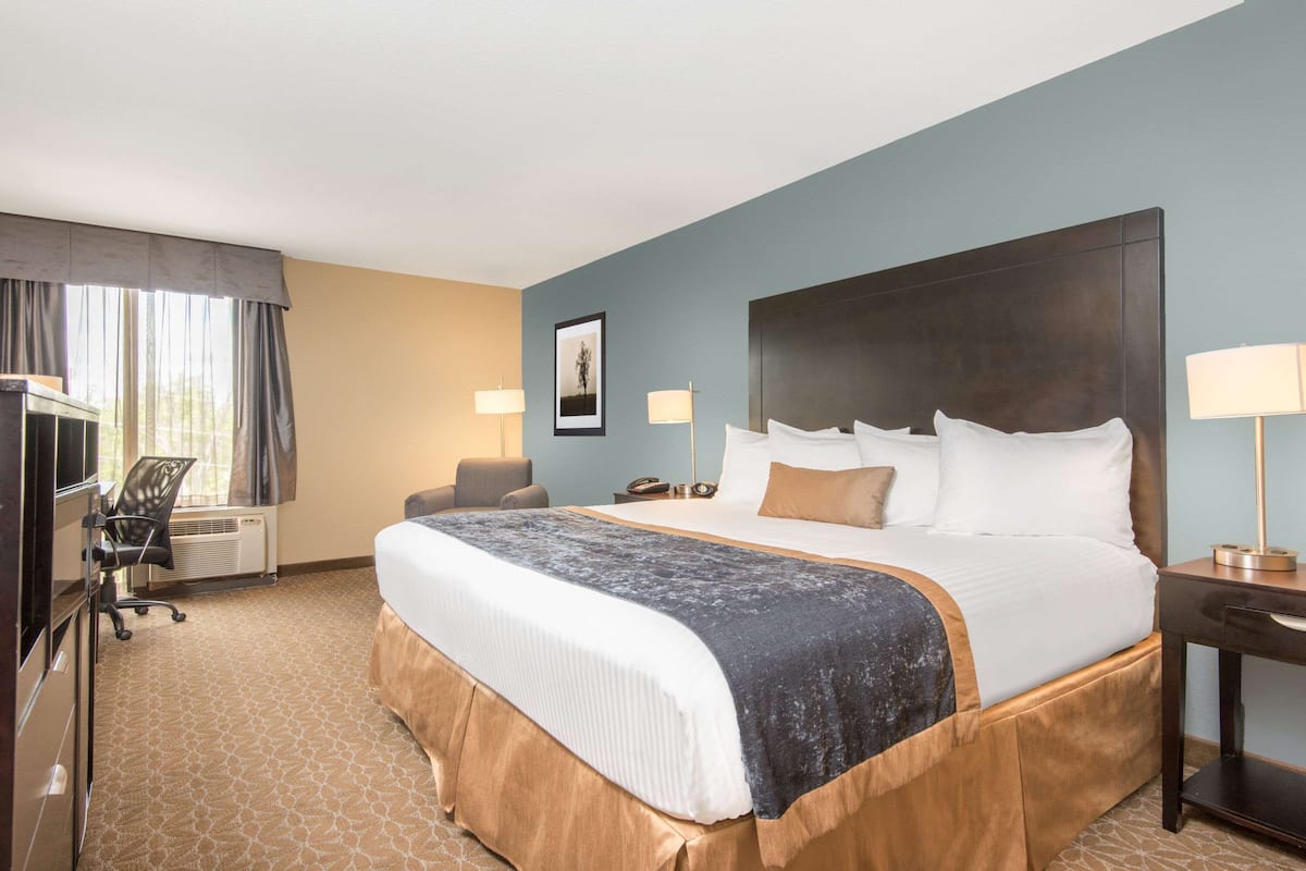 A hotel room with a large bed, a desk, a chair, and a desk lamp.