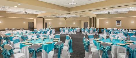 A large conference room with multiple round tables, each set with white chairs and teal tablecloths.