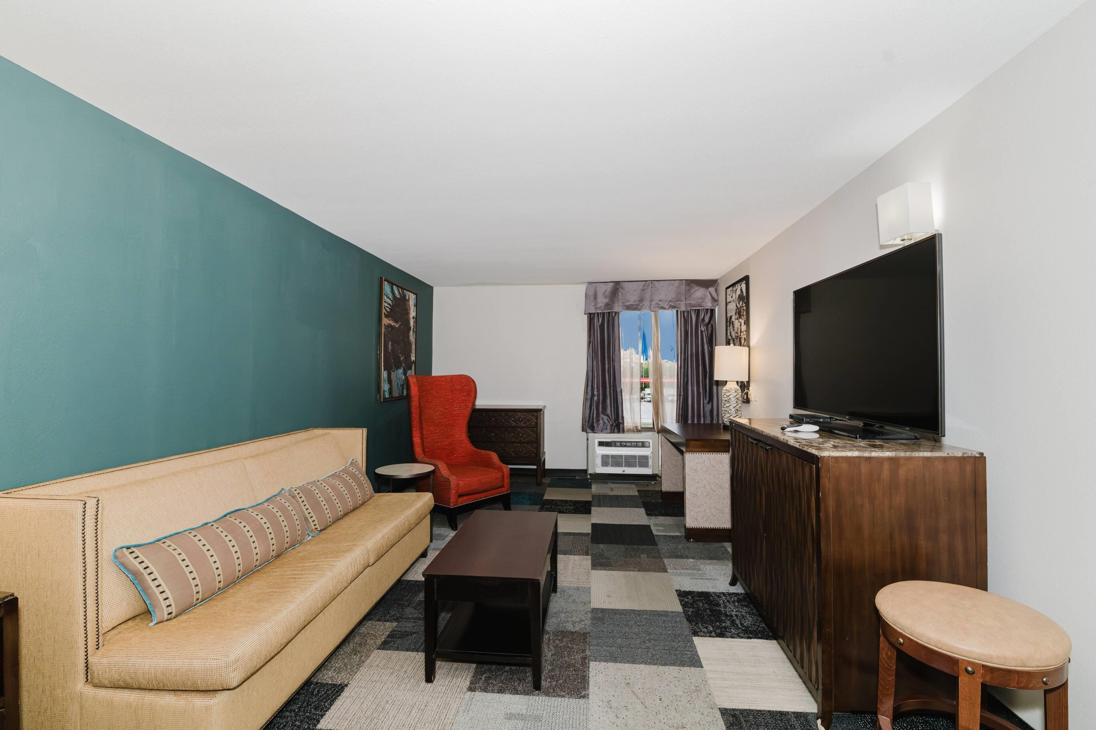 A living room with a sofa, a red armchair, a coffee table, a TV, and a small table with a lamp.