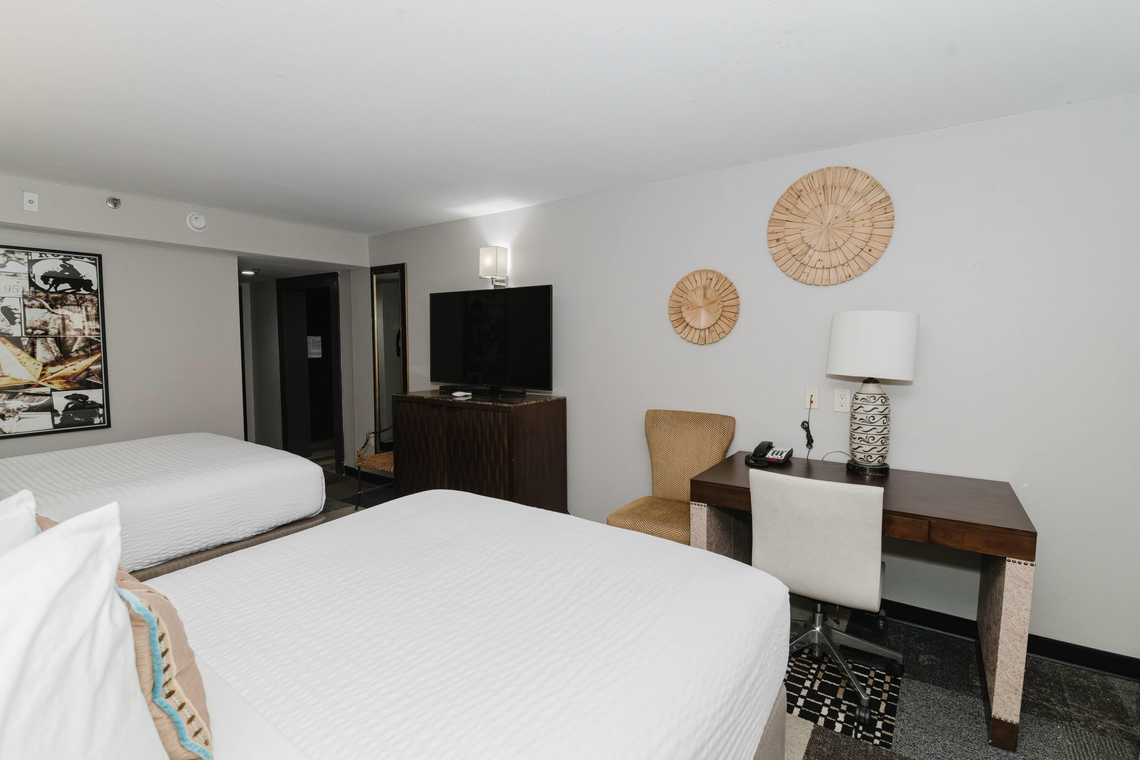 A hotel room with two beds, a desk, a chair, a television, and decorative wall art.