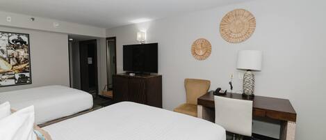 A hotel room with two beds, a desk, a chair, a television, and decorative wall art.