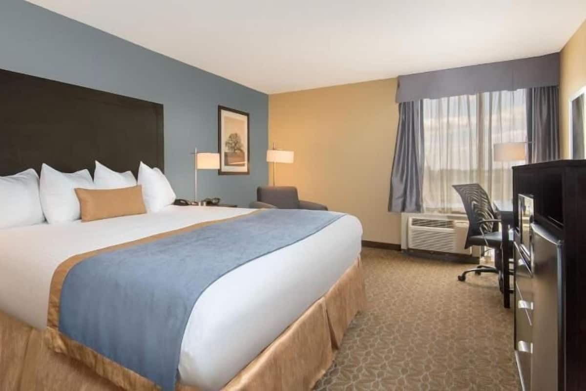 A hotel room with a large bed, bedside tables, a desk with a chair, a television, and a window with curtains.