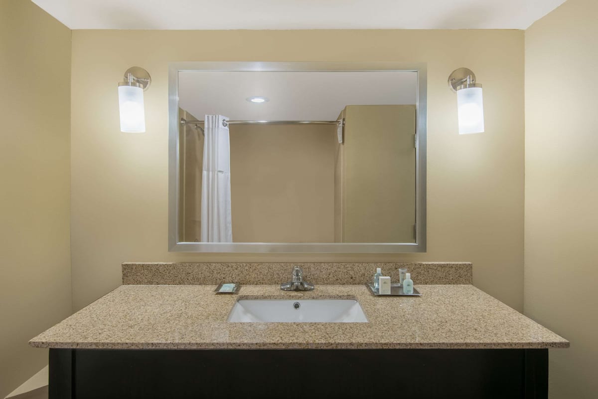 A bathroom with a large mirror, a sink, and two wall-mounted lights.