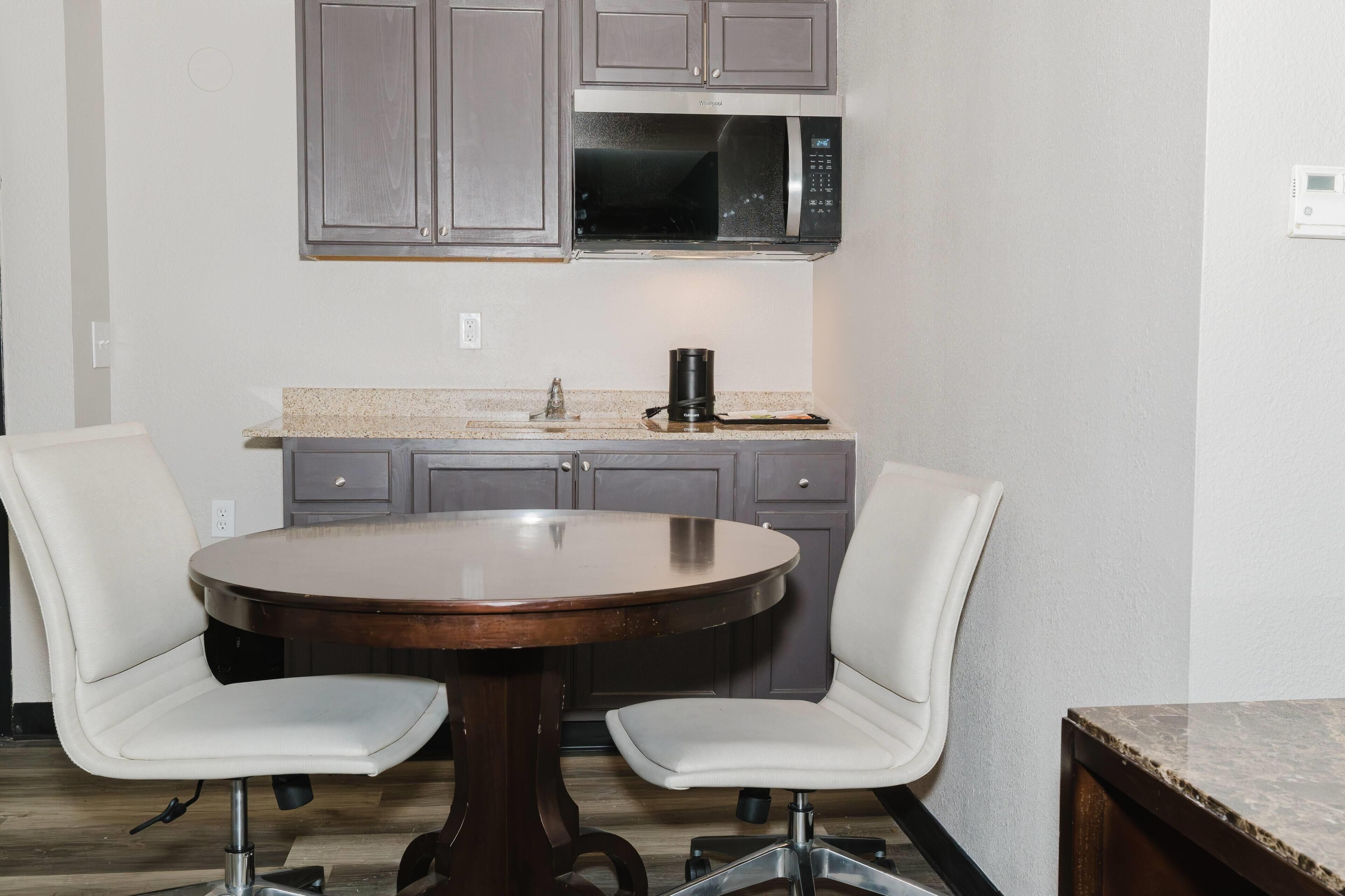 A kitchen with a round dining table, two chairs, a microwave, and cabinets.