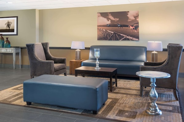Un hall d’entrée avec un canapé bleu, deux fauteuils, une table basse et une petite table ronde avec des lampes.
