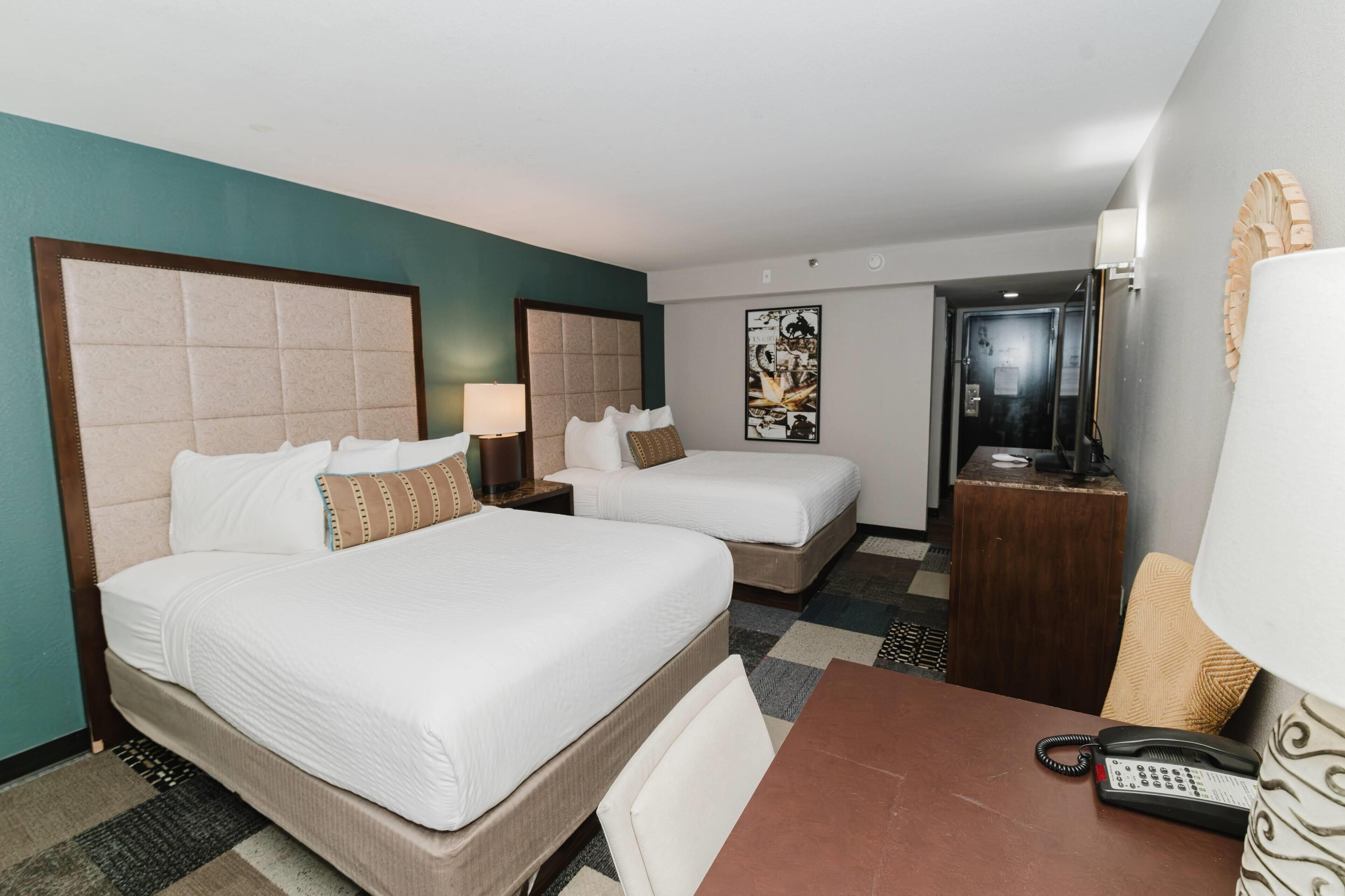 A hotel room with two beds, a desk, a telephone, and a door.