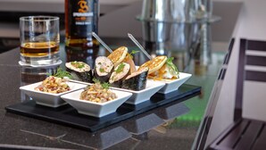 A bar area with a variety of liquor bottles, a glass of whiskey, and several dishes of food on the counter. - Hôtel Inn Paris CDG Airport (Roissy-en-France)