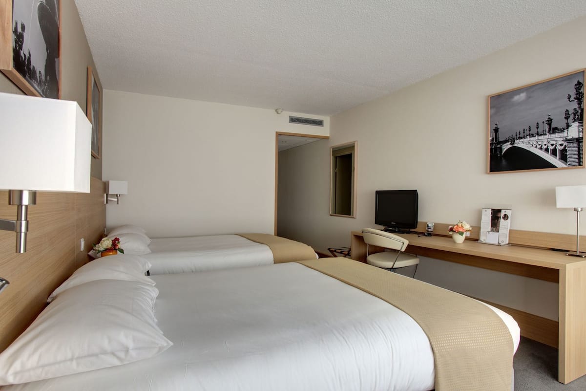Ein Hotelzimmer mit zwei Betten, einem Schreibtisch mit Computer, einem Fernseher und einem Spiegel.