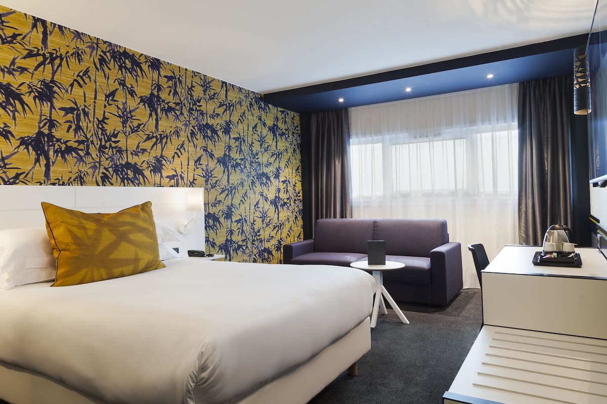 Ein Hotelzimmer mit einem großen Bett, einer Schlafcouch, einem Schreibtisch und einem Fenster mit Vorhängen.